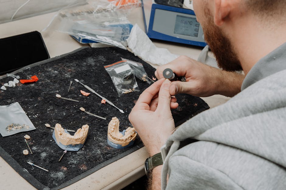 From above of crop anonymous male master sitting at table during creating denture and working with dental impression in modern dental clinic