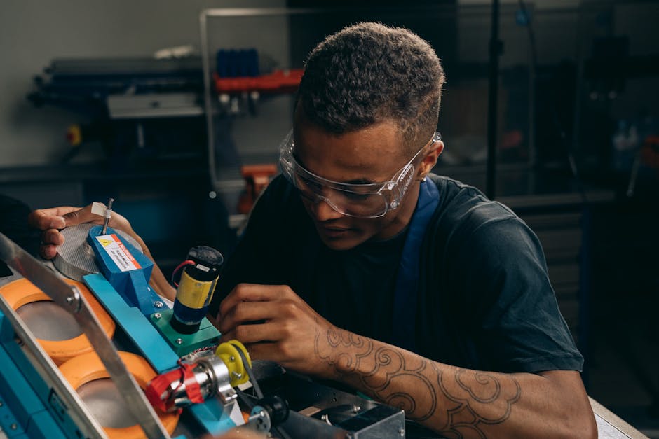 Focused young engineer wearing safety glasses adjusting machinery with precision in an industrial setting.